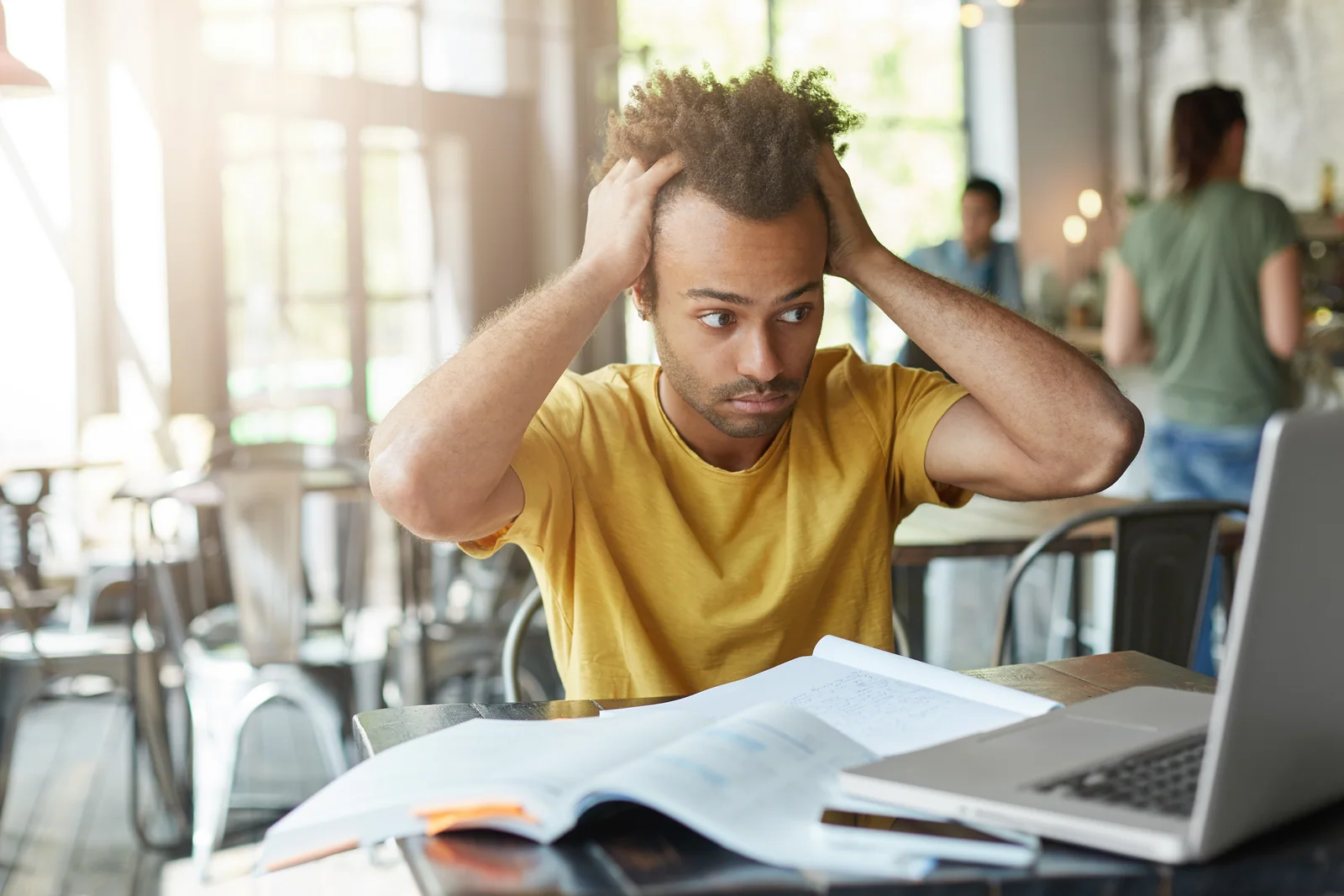 Stressed college student with hands on his head looking at a laptop, thinking: do my assignment