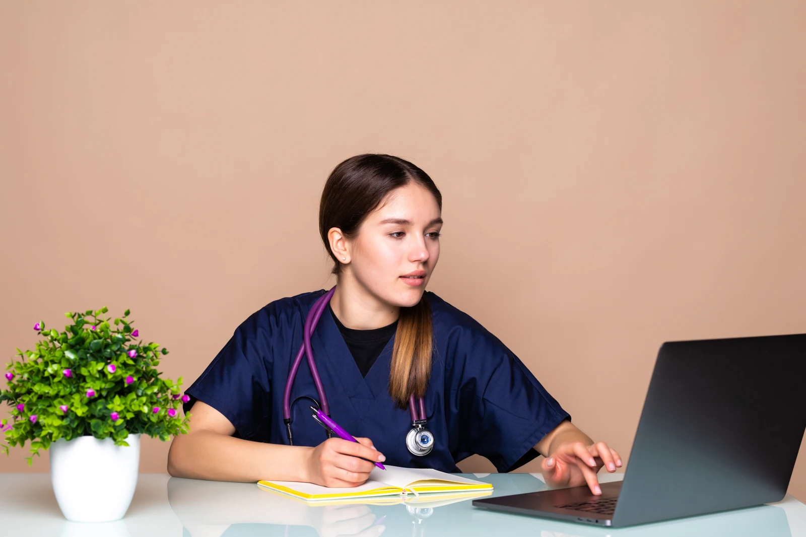 Nursing student in scrubs with a stethoscope working on a laptop